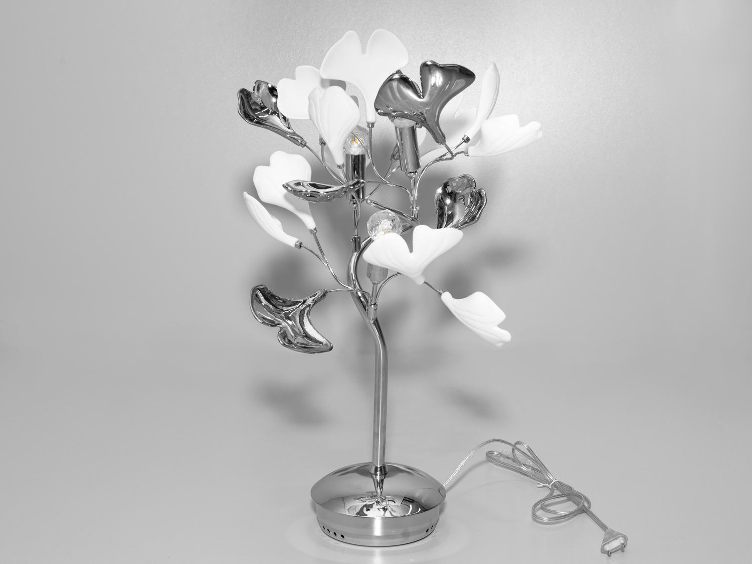 Приліжкова настільна лампа з керамічними елементами під три лампочки на тумбу/стіл є вершиною дизайнерської думки, де кожна деталь промовляє про вишуканість та стиль. Вона є частиною колекції, яка вже включає два варіанти вишуканої люстри, бра та стильний торшер, і продовжує естетичну лінію унікального дизайну, поєднуючи в собі античну витонченість та сучасну практичність. Лампа ідеально вписується в будь-який простір, створюючи гармонійне та затишне освітлення.
Серцем лампи є надійний металевий каркас з хромованим покриттям, який несе на собі керамічні елементи, що нагадують листя Гінкго Білоба, давній символ витривалості та сили природи. Неглазурований білий фарфор-бісквіт, з якого виготовлені пелюстки, має текстуру, що імітує мармур, додаючи лампі ауру класичної елегантності. Пелюстки, виконані в техніці глазурі під металік, варіюються від золотих до хромованих варіантів, що дозволяє їм вносити у дизайн нотки розкоші та блиску.
Компактна форма лампи на тумбу дозволяє їй легко вписатися в будь-яке дизайнерське рішення, будь то офісний стіл, куток для читання в домашній бібліотеці, або як стильний акцент на тумбочці в спальні. Три лампочки е14, встановлені в цю прикроватну настільну лампу, забезпечують м'яке, але достатньо яскраве світло для комфортної роботи або відпочинку, створюючи ідеальний баланс між функціональністю та естетикою.
Настільна лампа із кераміки ідеально підходить для інтер'єрів, де цінується симбіоз класики та модерну, де традиційні форми поєднуються з сучасними матеріалами, створюючи новітній вигляд класичних просторів. Фарфорова лампа також ідеально впишеться в інтер'єри стилів ар-нуво або ар-деко, де кожен елемент декору відіграє важливу роль у створенні неповторної атмосфери приміщення.
Ця настільна лампа служить стильним аксесуаром, що підкреслює вишуканість та унікальність інтер'єру, завдяки її скульптурній формі та деталям високої майстерності. Її присутність у просторі надає особливого відчуття розкоші та художньої цінності, змушуючи кожен погляд зупинятися на її витончених вигинах та грі світла.
Сучасна лампа на стіл, оригінальна лампа з вимикачем, ексклюзивна прикроватна настільна лампа з керамічними елементами на 3 лампи, керамічні лампи, купити незвичну настільну лампу, нічна лампа, лампа настольна Харків, лампа арт деко.
Лампи в комплект не входять.